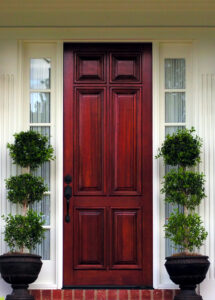 large, dark wood entry door with potted plants on either side of it